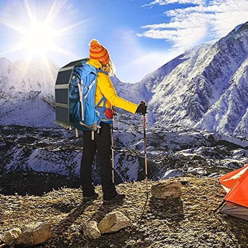 Senderista en alta montaña con el panel solar BigBlue 28W desplegado y enganchado a la mochila mientras camina hacia una tienda de campaña